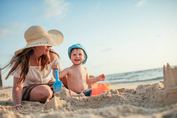 мать и сын на пляже играют с песком - sandcastle стоковые фото и изображения