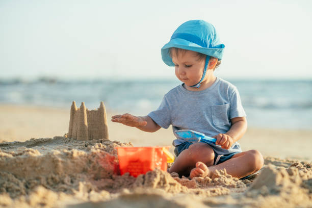 счастливый маленький мальчик здание песчаный замок на пляже - lifestyles child beach digging стоковые фото и изображения