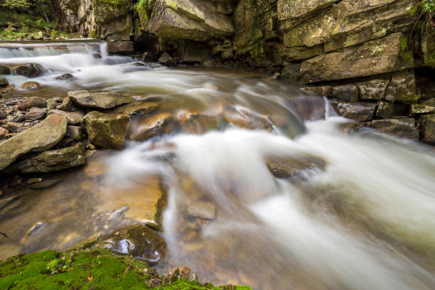 istock Fast flowing river stream with smooth silky water falling from big stones in beautiful waterfalls on bright sunny summer day. 1159167329
