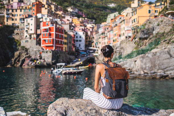 Enjoying the view. Female tourist relaxing by the sea. She is looking at the beautiful town Riomaggiore, Cinque Terre spezia stock pictures, royalty-free photos & images