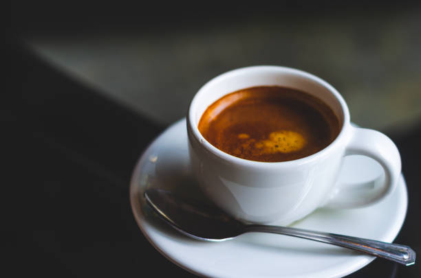 istock close up modern hot black coffee the espresso on dark background with coffee bubble foam pattern and texture in white cup looking and feel so delicious on glasses table in coffee shop. 1159172061