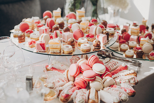 Delicious pink candy bar at wedding reception. Pink and white desserts,macarons and cupcakes on stand, modern sweet table at wedding or baby shower. Luxury catering concept