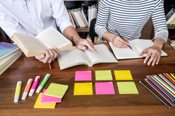 istock Education, teaching, learning concept. Two high school students or classmates group sitting in library with helps friend doing homework and lesson practice preparing exam to entrance 1159177896