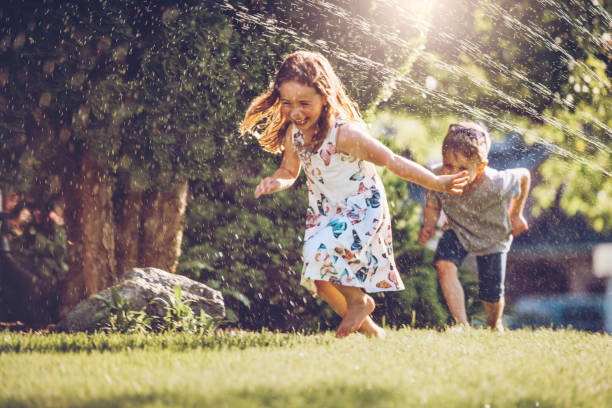 gosses heureux jouant avec l'arroseur de jardin - child family offspring fun photos et images de collection