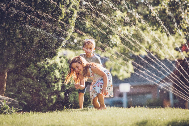 istock Happy kids playing with garden sprinkler 1159180352