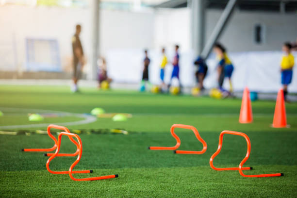 istock orange hurdles on green artificial turf with blurry coach and kid soccer are training. 1159180724