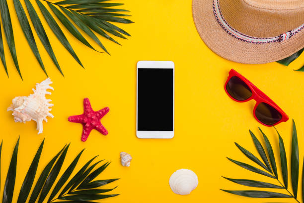 istock Hat, tropical palm leaves, sunglasses, sea shells and smartphone on yellow background. 1159181702