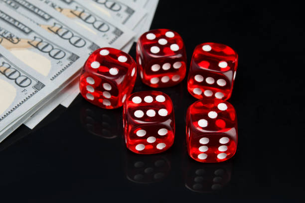 istock on a black background with a reflection, five red dice for the game and hundred dollar bills laid out in a row 1159183512