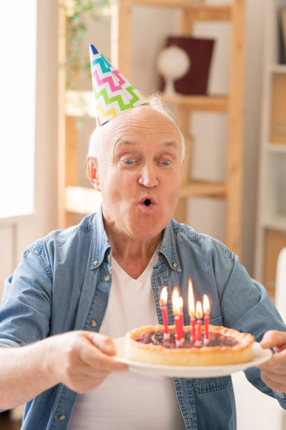 istock Aged man blowing candles on homemade birthday cake 1159183838