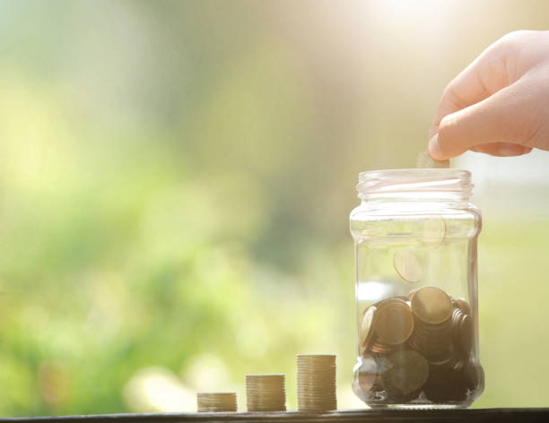istock Man hand dropping coin and coins and jar. 1159189174