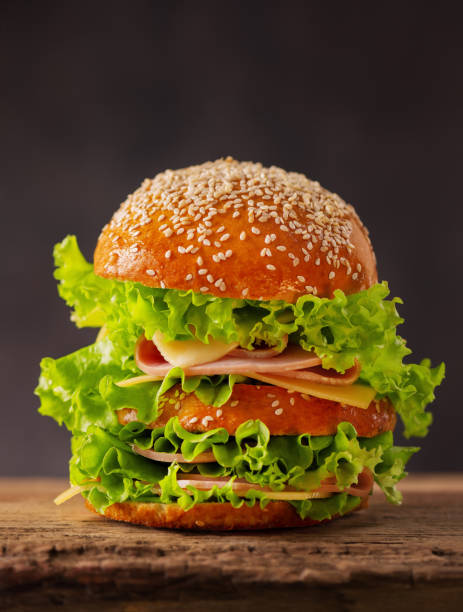 istock Big sandwich burger with cheese, ham and lettuce on a dark background. 1159193520
