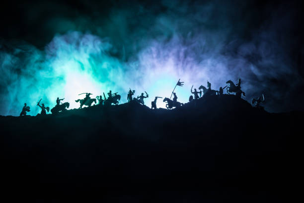 istock Medieval battle scene with cavalry and infantry. Silhouettes of figures as separate objects, fight between warriors on dark toned foggy background with medieval castle. 1159197533
