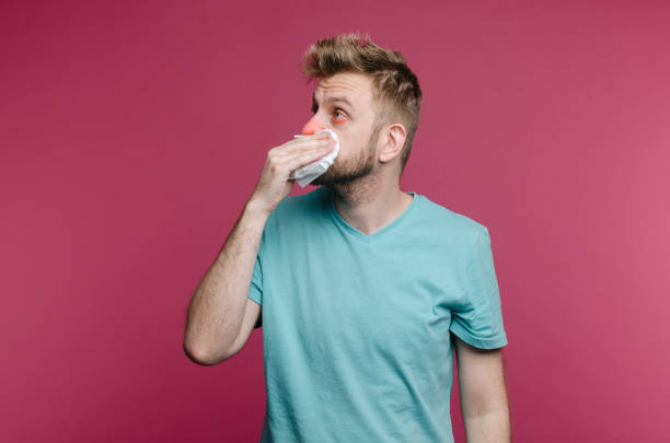 istock studio picture from a young man with handkerchief. Sick guy isolated has runny nose. man makes a cure for the common cold 1159198981