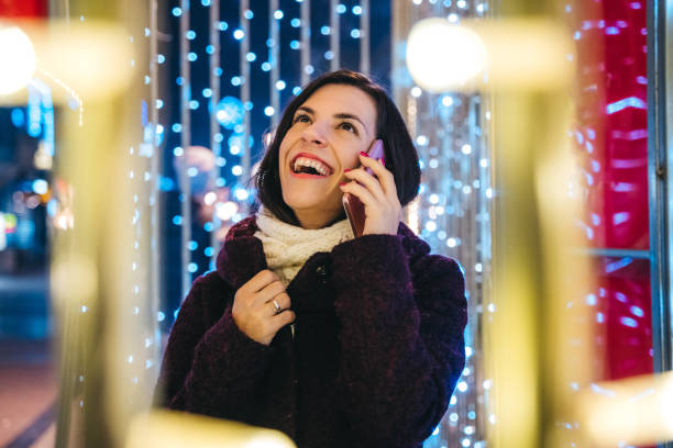 istock Woman talking over phone among Christmas lights 1159200034