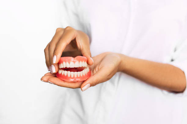 prótesis dental en manos del primer plano del médico. dentista sosteniendo puente dental de cerámica. vista frontal de la dentura completa. foto conceptual de la odontología. odontología protésica. dientes falsos - colmillo fotografías e imágenes de stock