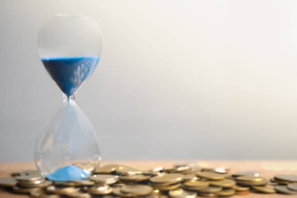 istock Hourglass blue sand and stack of coins. 1159202998