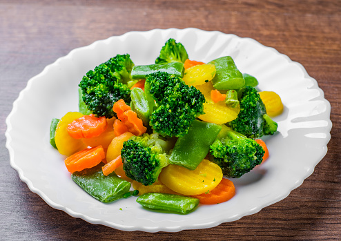 Mixed vegetables. green bean, broccoli and carrots in white plate on a wooden table background.