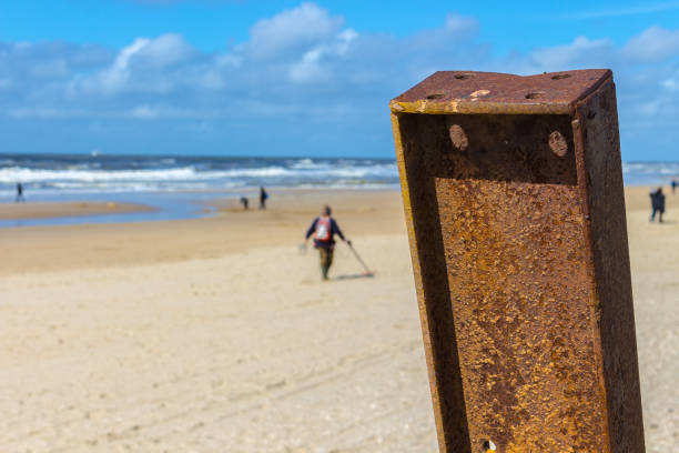 istock Rusty pole on the beach, guy with metal detector in the blurry background, walking over the north sea beach in northern holland. 1159206833