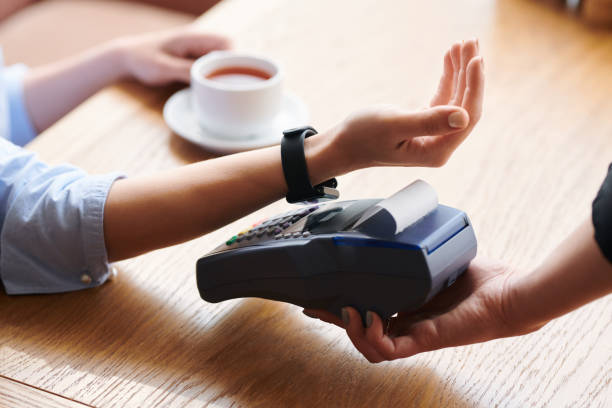 Making contactless payment with smartwatch Close-up of unrecognizable woman putting wristwatch to payment terminal while making contactless payment in cafe smart watch business stock pictures, royalty-free photos & images
