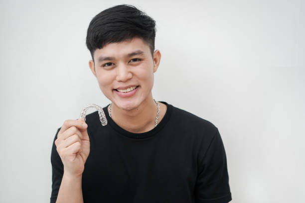 крупным планом (изолированный) молодой азиатский человек улыбается с рук, держа сто�матологический выравниватель (невидимый) на белом фоне � - dentist asian ethnicity portrait male стоковые фото и изображения