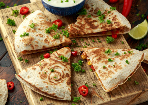 istock Mexican quesadilla with chicken, corn, black beans, cheese, vegetables, lime and yogurt sauce on wooden board 1159212523
