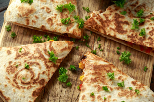 istock Mexican quesadilla with chicken, corn, black beans, cheese, vegetables, lime and yogurt sauce on wooden board 1159212570