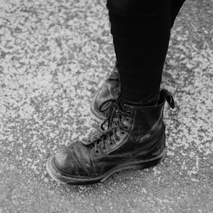 Black and white photo of a pair of dirty black boots on asphalt.