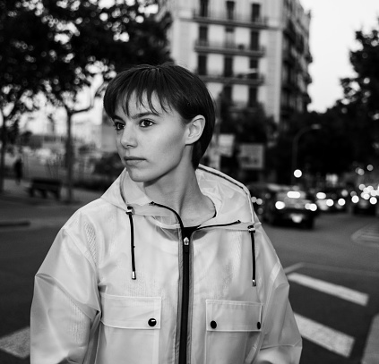 Portrait of a casual young girl wearing a translucent raincoat in Barcelona streets. Black and White.