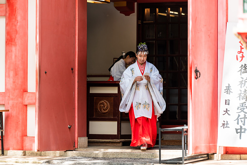 Nara, Japan - April 14, 2019: People woman in traditional costume at shinto shrine Kasuga jinja with red and white dress walking by door