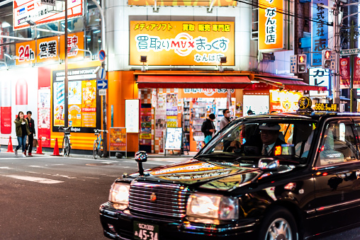 Osaka, Japan - April 13, 2019: Minami Namba street with illuminated buildings colorful signs and black taxi cab in traffic