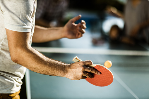 Close up of unrecognizable man having fun while playing table tennis outdoors.