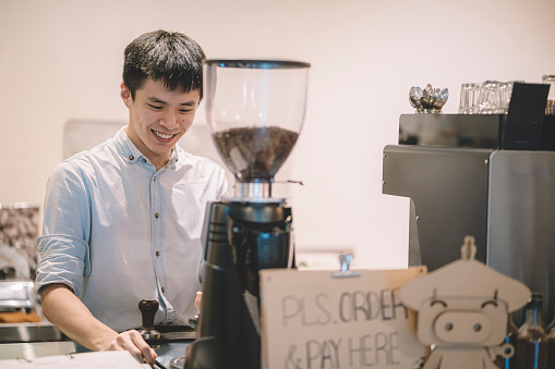Barista making, preparing and grinding Cappuccino in Coffee Shop with smiling face