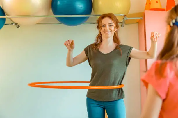 Fun exercise. Happy positive woman smiling while rotating a hula hoop