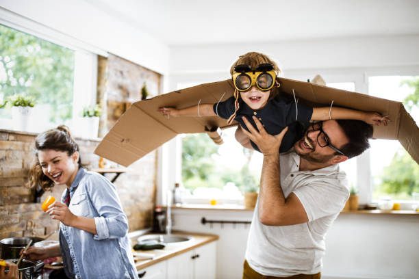 Look daddy, I'm an airplane! Happy boy pretending to be an airplane and looking at camera while his father is holding him in dining room. arms outstretched photos stock pictures, royalty-free photos & images