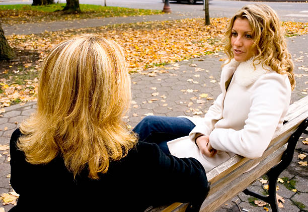 A mother and daughter share thoughts and feelings on a park bench in the autumn.