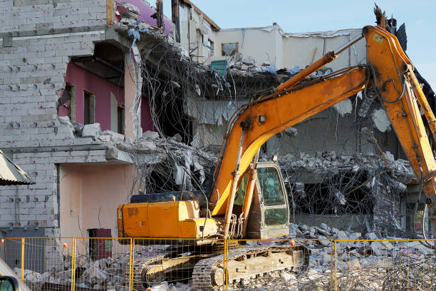 Yellow excavator demolishing a multi-storey building. Destroyed floors of the building, are pieces of stone, concrete, fittings. Construction equipment on stones and fixtures. Yellow excavator demolishing a multi-storey building. Destroyed floors of the building, are pieces of stone, concrete, fittings. Construction equipment on stones and fixtures. dismantling photos stock pictures, royalty-free photos & images