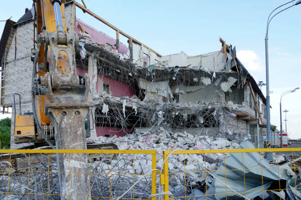 istock Ruined multi-storey building. An excavator demolishes a multi-storey building with a chisel tool. Technique destroys the building, is fittings, concrete and stones. The fence of the yellow fence. 1159223963