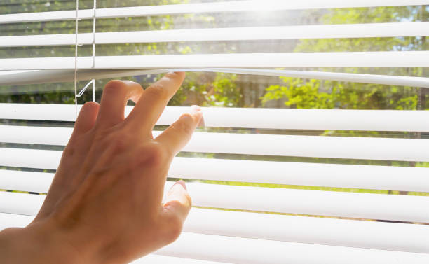 istock hand opens with fingers blinds, outside window there is sunlight and green trees. Concept hot summer and scorching sun 1159226493