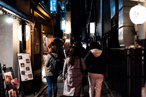Kyoto, Japan - April 16, 2019: People walking on Pontocho alley district street at night with illuminated lanterns and izakaya restaurant menu