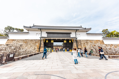 Kyoto, Japan - April 17, 2019: City street wide angle view during day morning of entrance to Nijo castle with people walking and guards