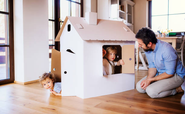 Two toddler children with father playing with paper house indoors at home. Two happy toddler children with father playing with paper house indoors at home. cardboard house stock pictures, royalty-free photos & images