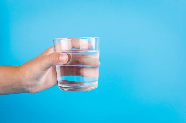 istock glass of water in hand on blue 1159236326