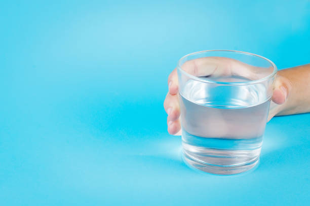 istock glass of water in hand on blue 1159236329