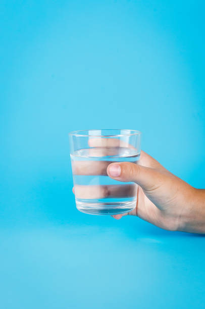 istock glass of water in hand on blue 1159236770
