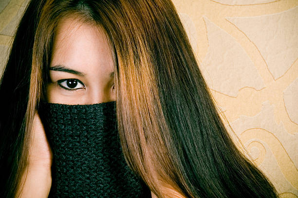 Asian Girl hiding behind her sweater with intense eyes into the camera.
