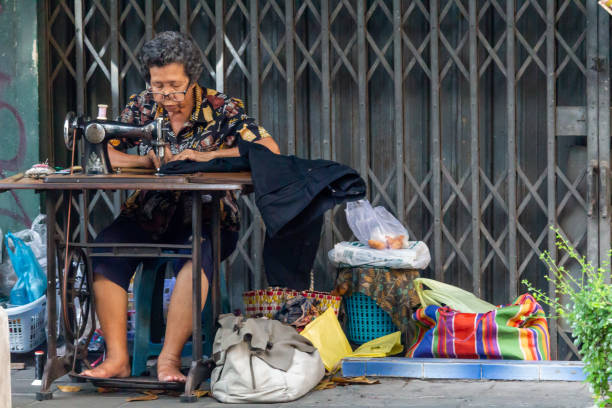 Bangkok, Thailand - April 12, 2019: Barefoot senior woman sewing on a street in Bangkok