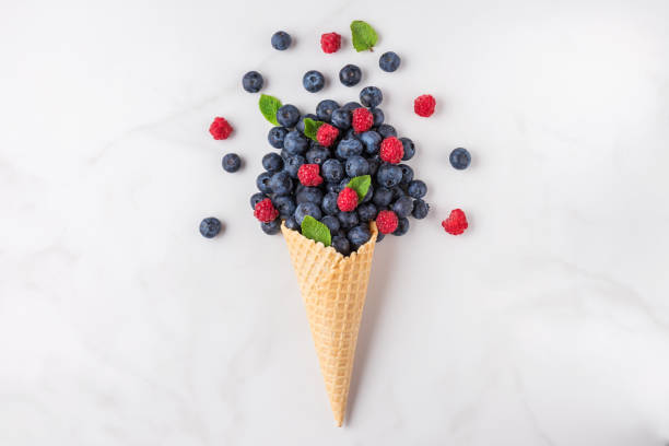 istock wild berries blueberry and raspberry with mint in waffle ice cream cone on white marble background. summer food concept 1159249216