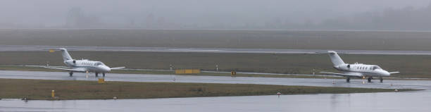 due jet privati su un panorama aeroportuale piovoso - runway airport rain wet foto e immagini stock
