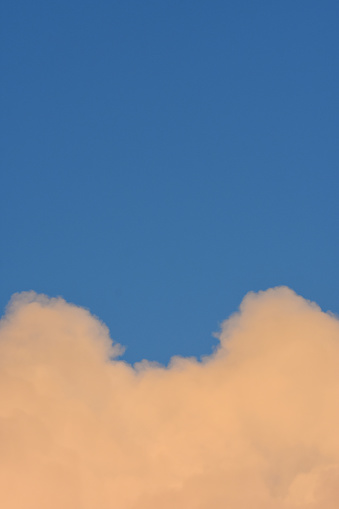 Dusk colors on rising cloud with two peaks against the frame edges and blue sky in the background. Photo taken in Jupiter, Florida. Nikon D7200 with Nikon 200mm macro lens.