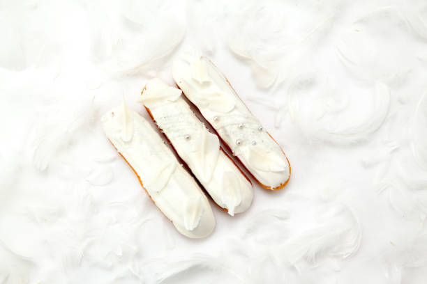 A set of three eclairs with white chocolate decor isolate on a white surface decorated with white feathers